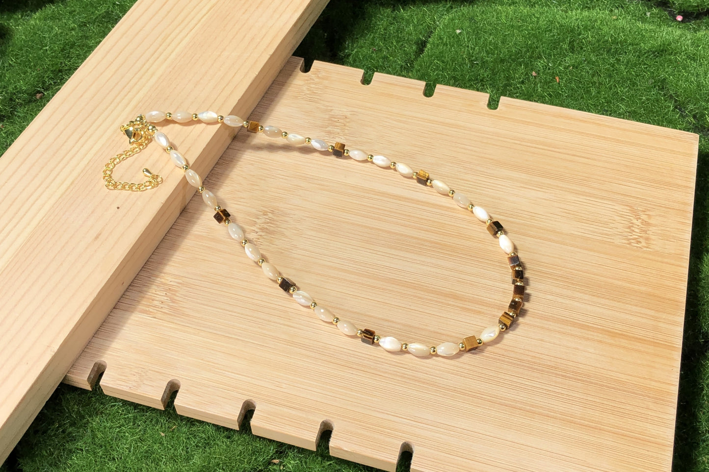 Eine handgefertigte Halskette mit Muschel- und natürlichen Tigeraugen-Würfelperlen und einer 14-karätig verkupferten Goldkette.