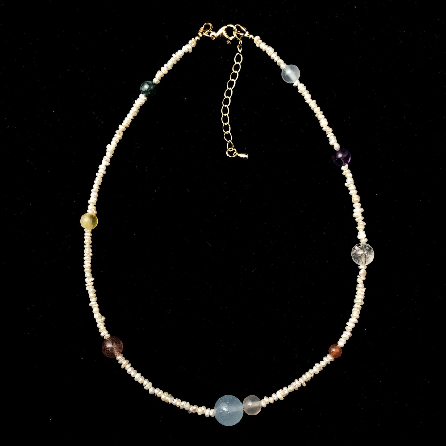 Eine handgefertigte Halskette mit natürlichen Süßwasserperlen und farbigen Edelsteinen, die die acht Planeten darstellen.