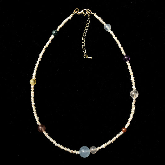 Eine handgefertigte Halskette mit natürlichen Süßwasserperlen und farbigen Edelsteinen, die die acht Planeten darstellen.