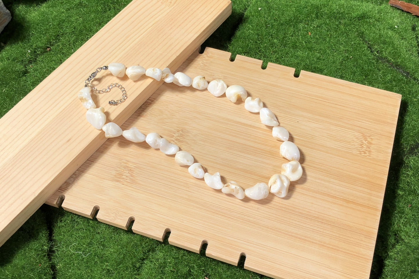 Eine unregelmäßige, handgefertigte Halskette aus weißen Muscheln mit einer Silberkette.