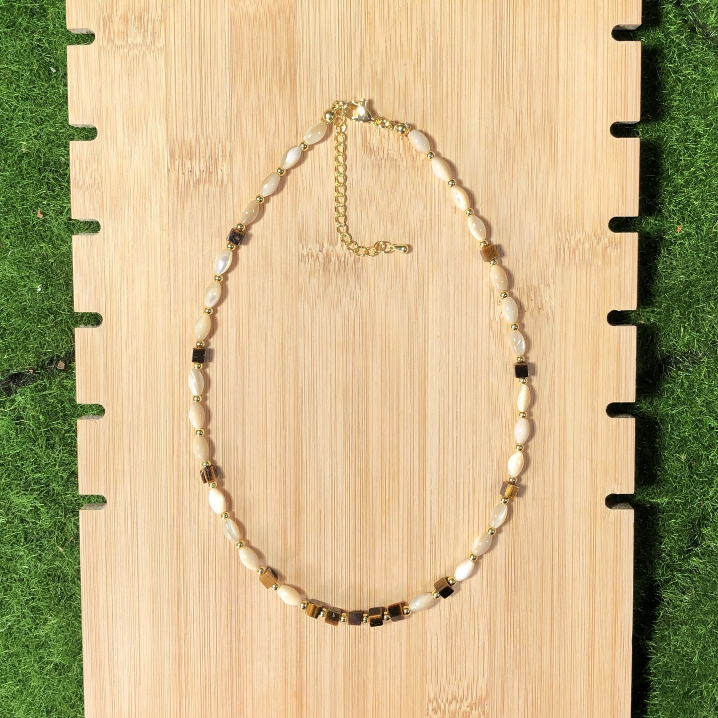 Eine handgefertigte Halskette mit Muschel- und natürlichen Tigeraugen-Würfelperlen und einer 14-karätig verkupferten Goldkette.