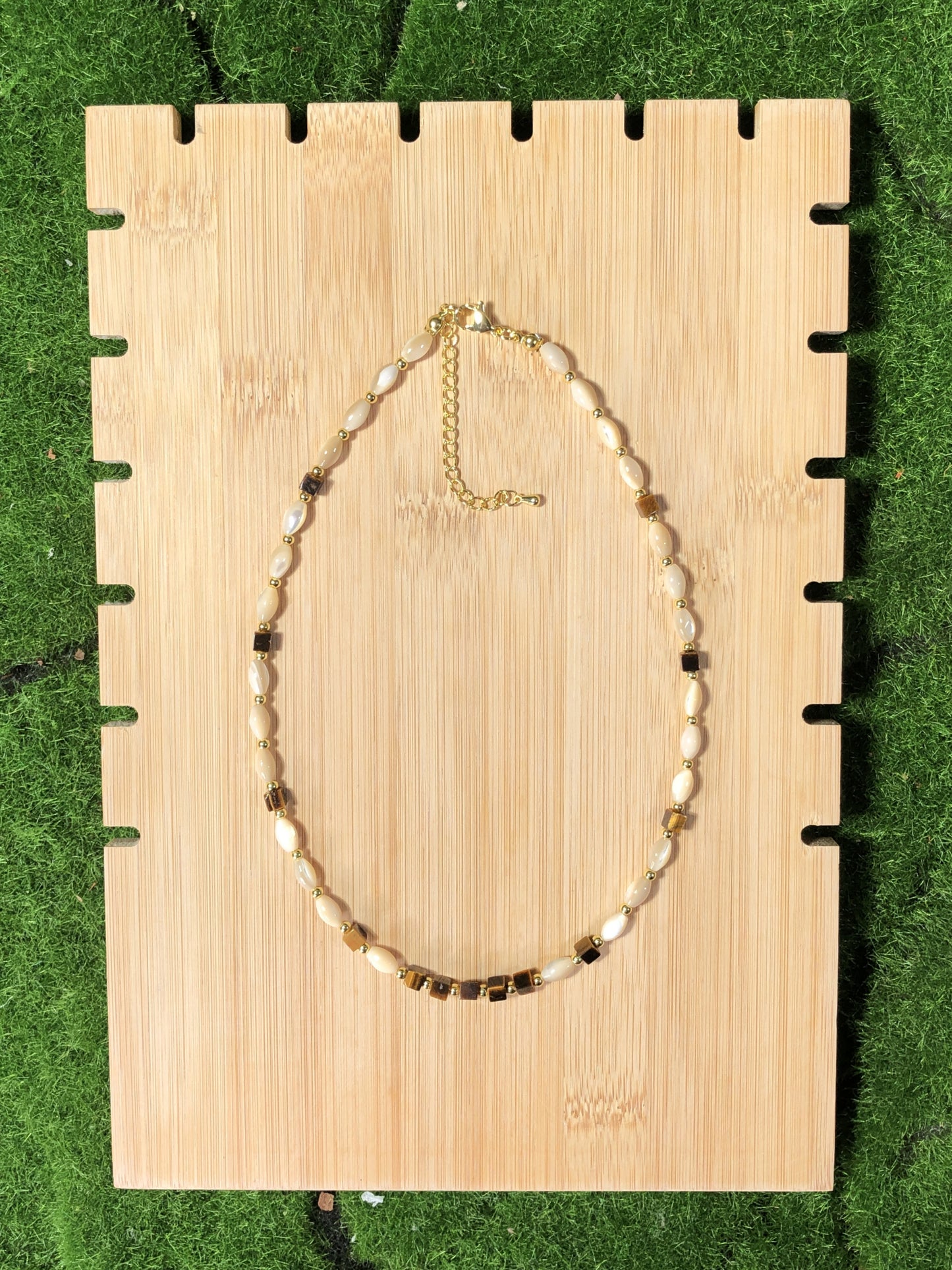 Eine handgefertigte Halskette mit Muschel- und natürlichen Tigeraugen-Würfelperlen und einer 14-karätig verkupferten Goldkette.