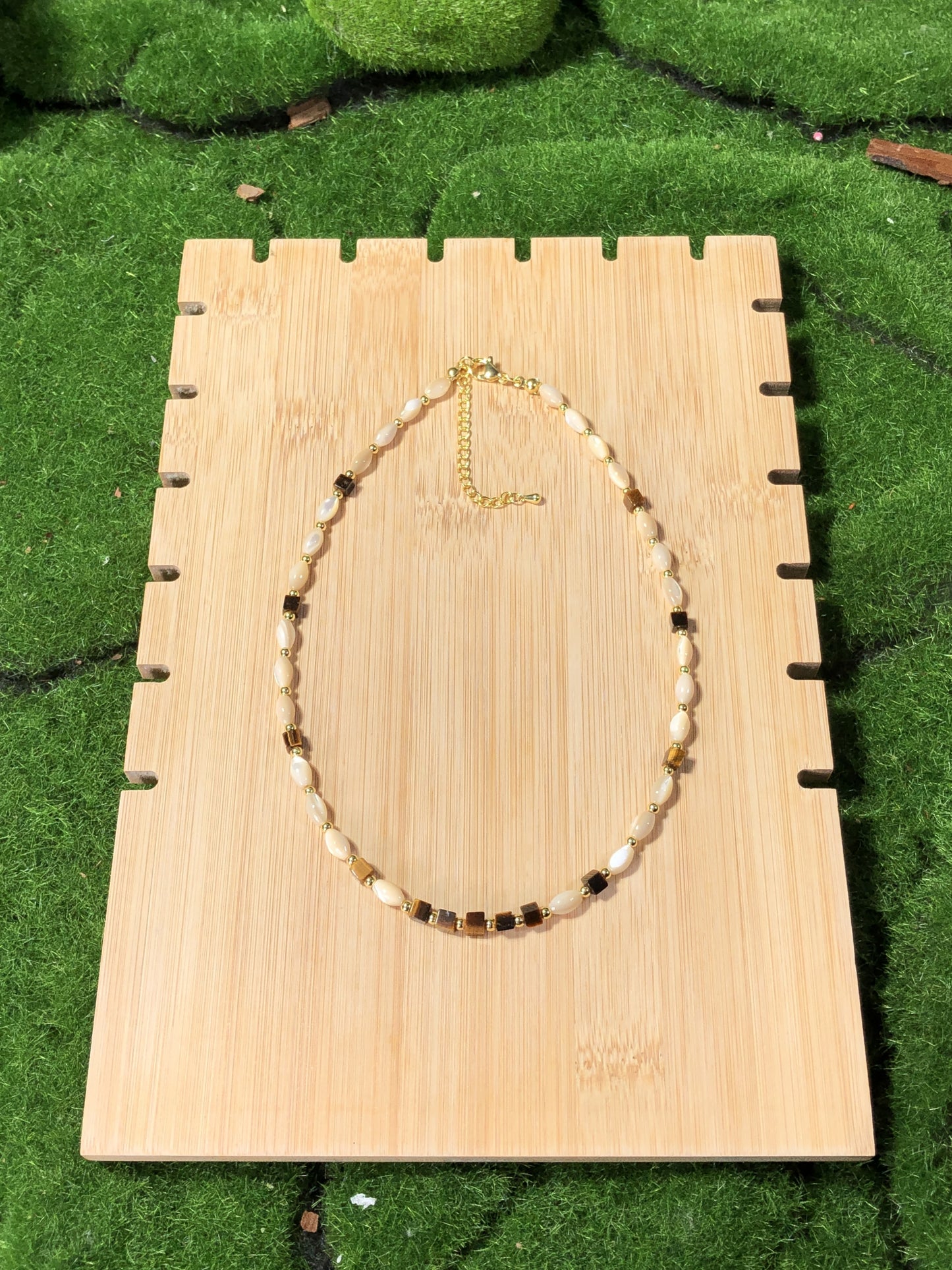 Eine handgefertigte Halskette mit Muschel- und natürlichen Tigeraugen-Würfelperlen und einer 14-karätig verkupferten Goldkette.