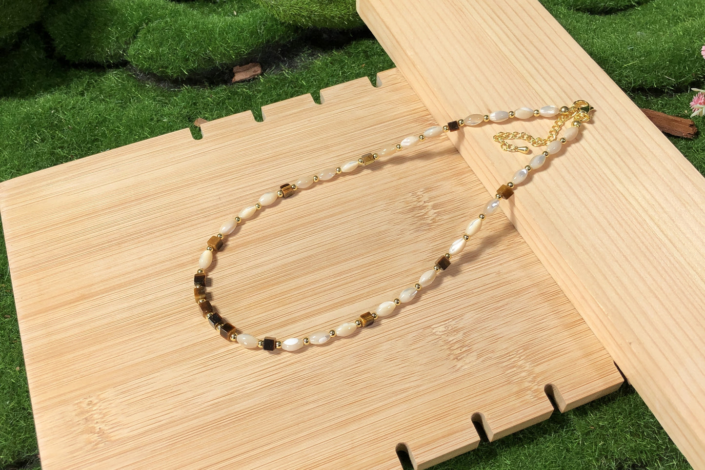 Eine handgefertigte Halskette mit Muschel- und natürlichen Tigeraugen-Würfelperlen und einer 14-karätig verkupferten Goldkette.